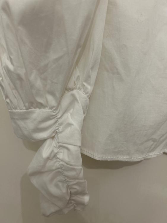 Detail of a white blouse with puffed and ruched sleeves, showing soft texture and visible seams.