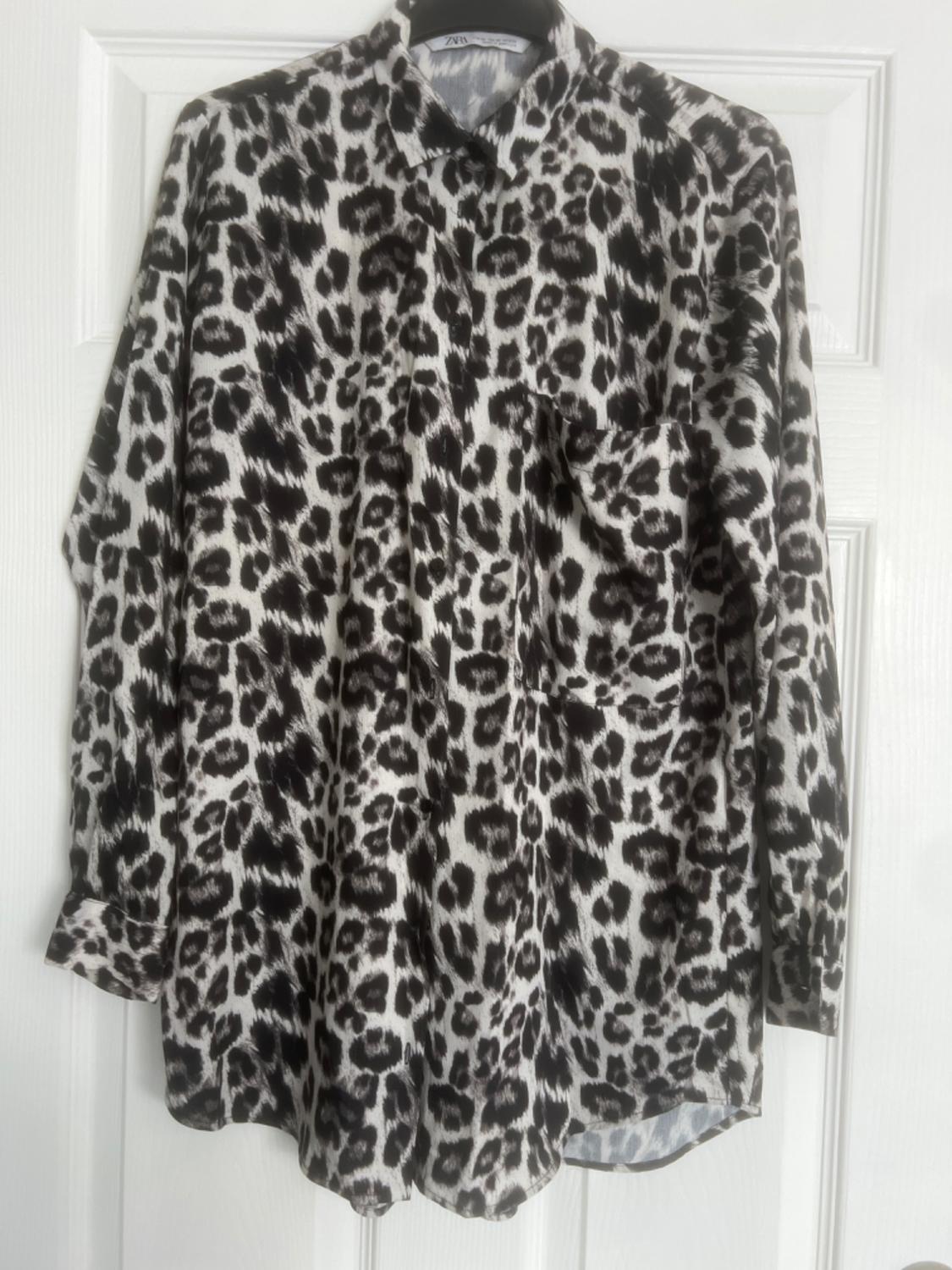 Long-sleeved shirt with black and white leopard print, hanging on a white door.