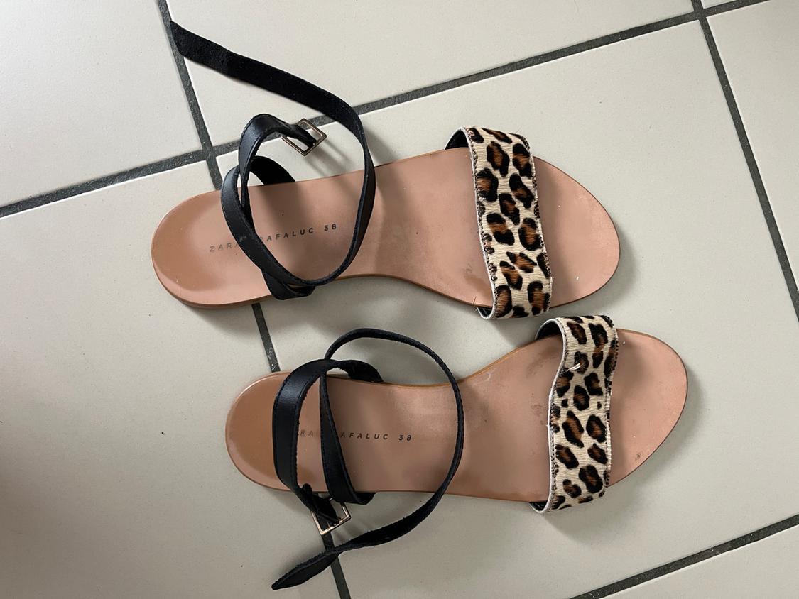 Top view of flat leopard print sandals with black straps on white tiles. Text: ZARA TRAFALUC 38.