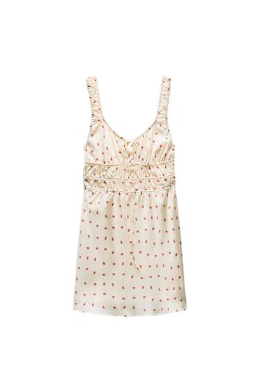 Front view of a cream dress with ruched straps and a small red floral print.