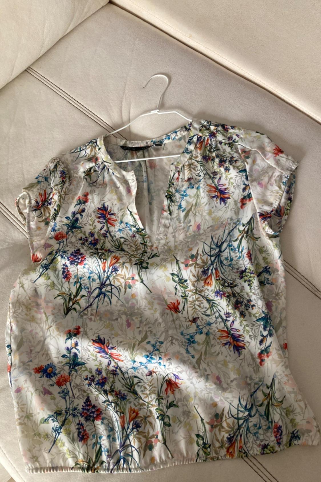 Front view of a floral blouse with a V-neck and short sleeves, featuring a multicoloured floral print on a light background.