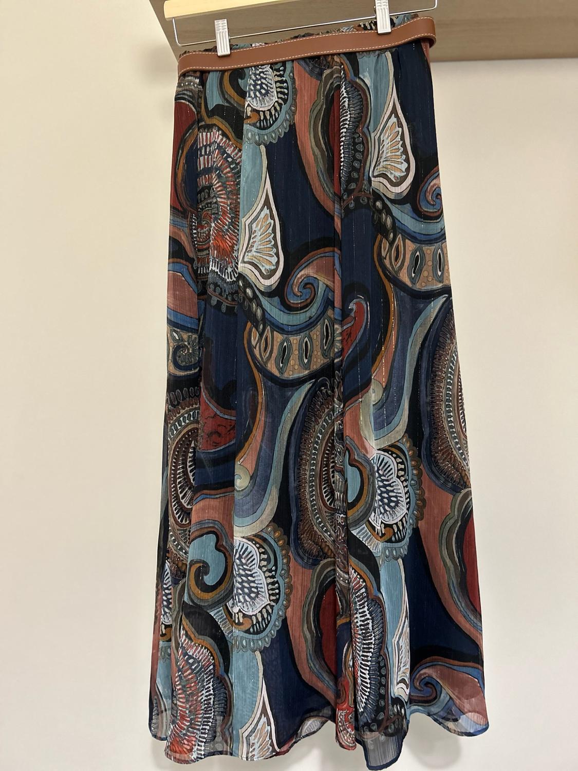 Flowing maxi skirt with an abstract print in shades of blue and brown, hanging from a hanger with a brown belt against a light background.