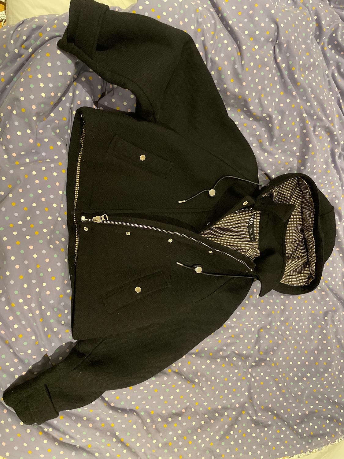 Black hooded zip-up jacket on a purple duvet with colourful polka dots.