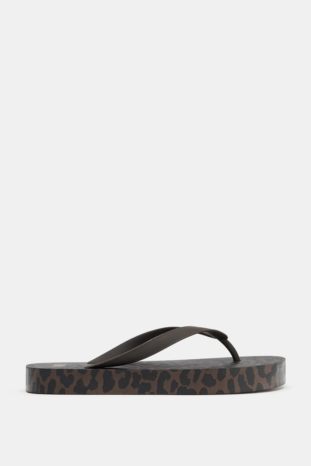 Side view of a sandal with an animal print on the sole and black straps.