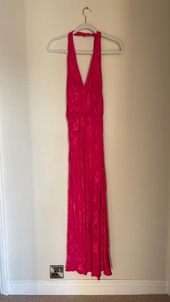 Fuchsia maxi dress with a V-neckline hanging on a white hanger against a beige wall.