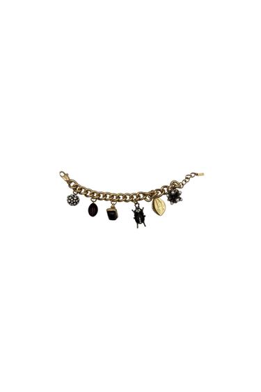 Gold bracelet with assorted charms: sphere with stones, red oval, black cube, scarab, gold leaf, and silver flower. White background.