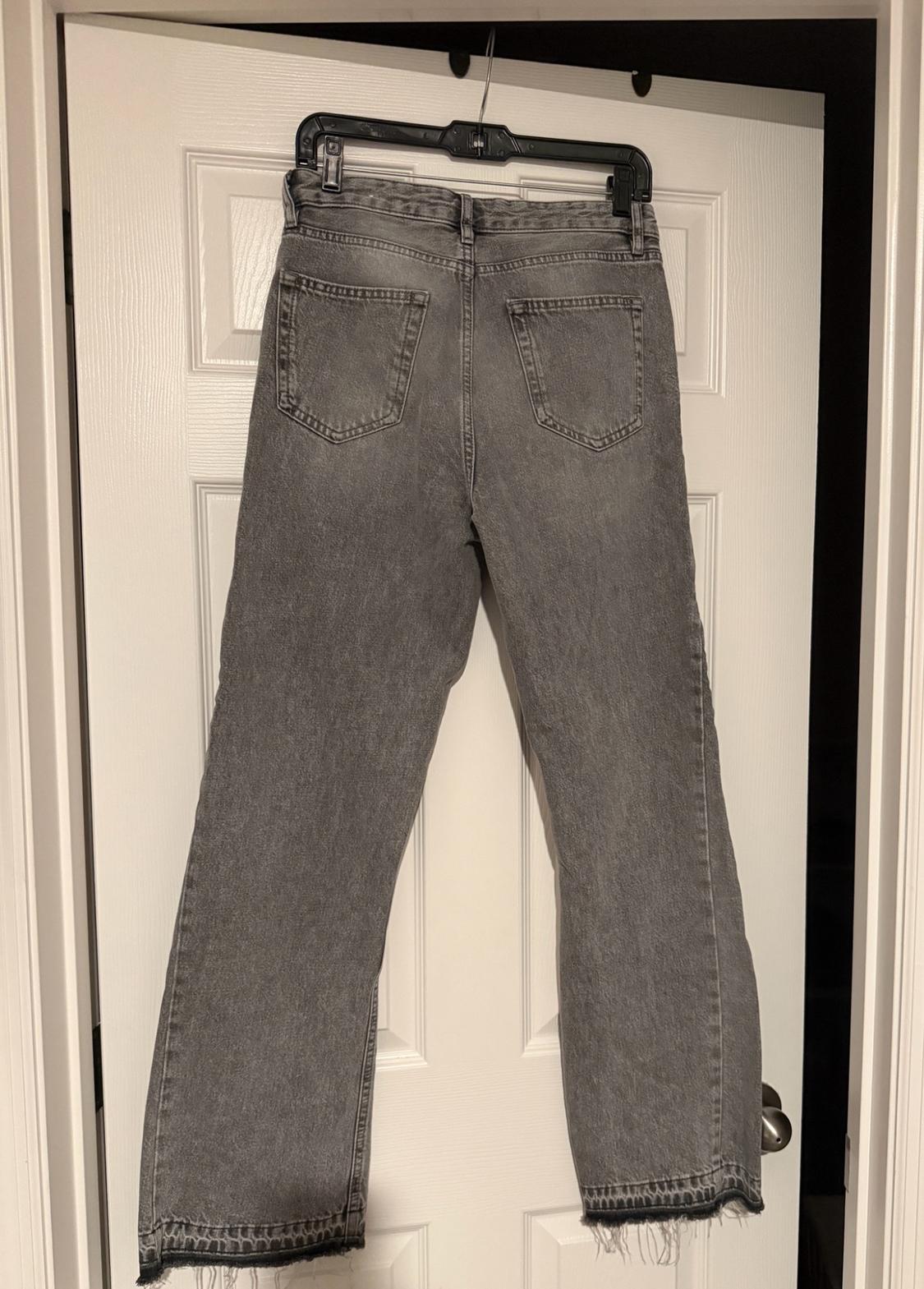 Gray jeans hanging from a hanger on a white door. Rear view with pockets and a frayed hem.