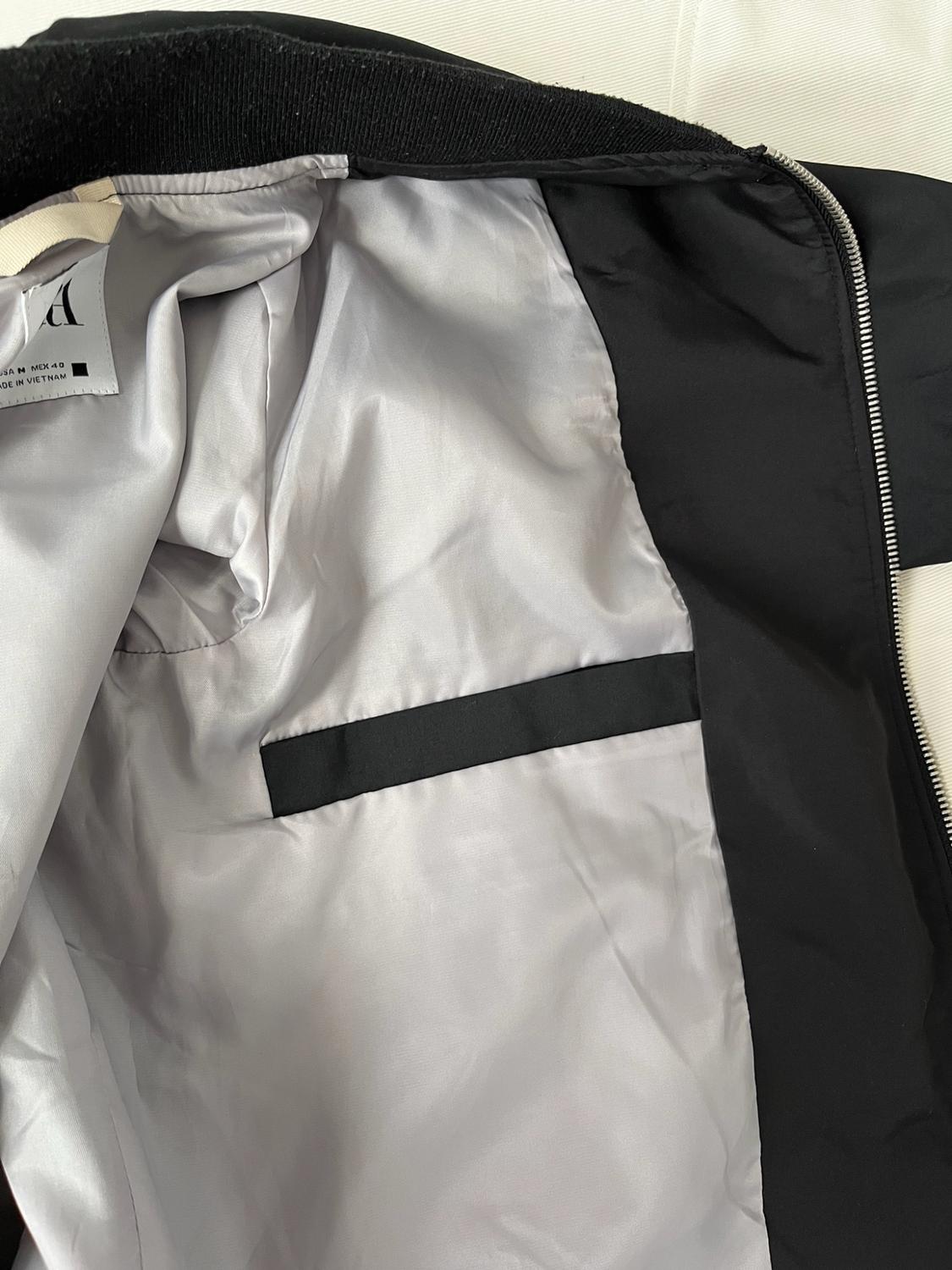 Interior of a black jacket with light grey lining, zip and inside pocket. Text: A USA M MEX 40 MADE IN VIETNAM.