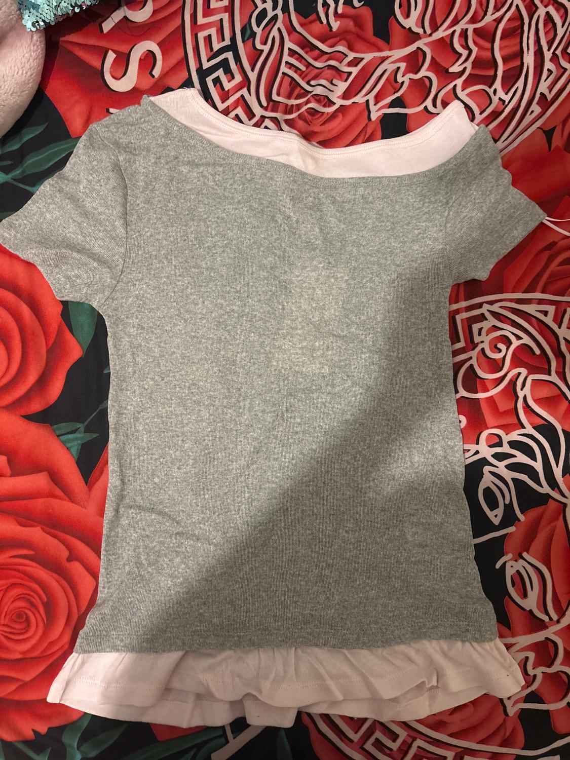 Grey T-shirt with a white collar and hem on a red bedspread with a rose design and geometric patterns.