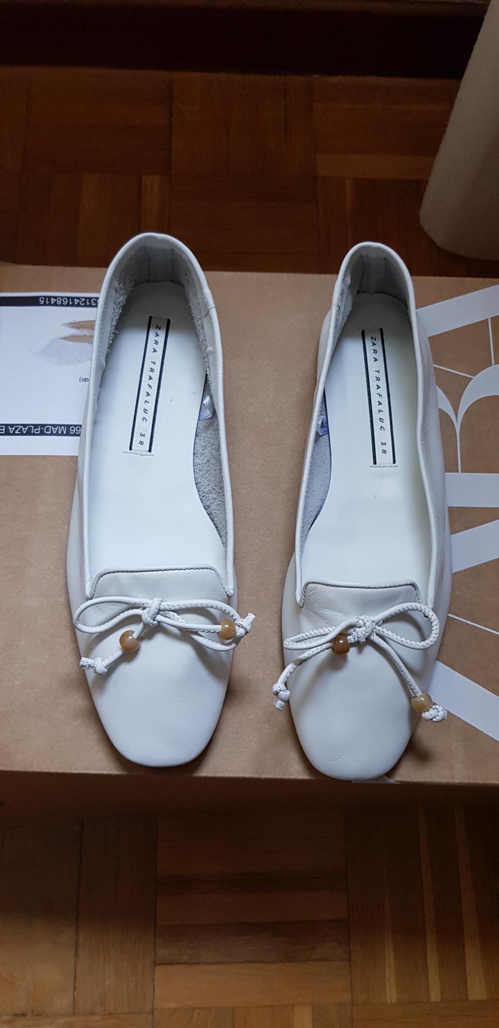 White shoes with a bow and brown beads on a cardboard box.