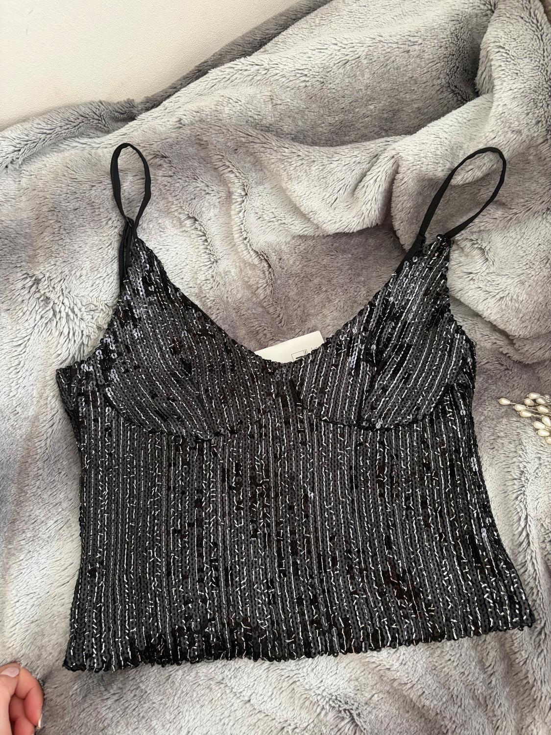Black sequin camisole on a grey blanket. Shimmering vertical stripe design. Cosy and elegant atmosphere.