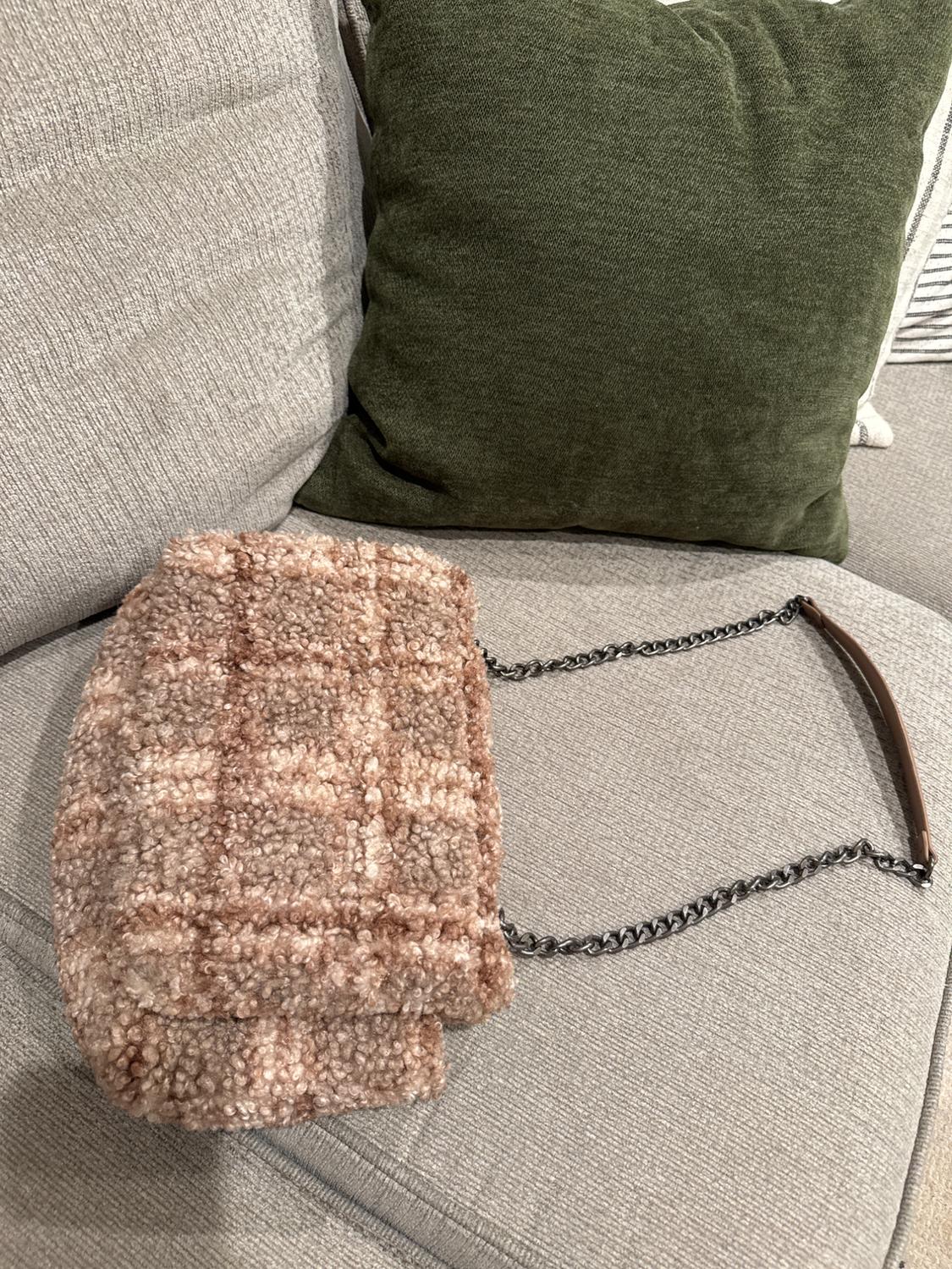 Light brown textured fabric handbag with a metallic chain on a grey sofa and dark green cushion.