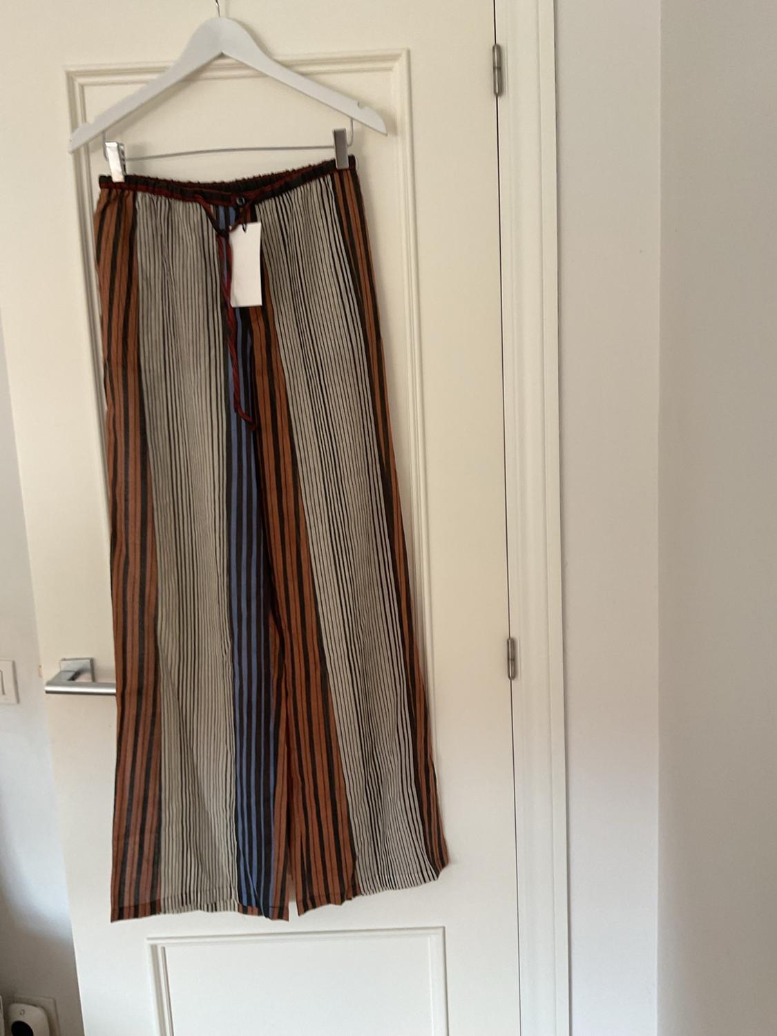 Flowing trousers with vertical brown, white, black and blue stripes, hanging from a hanger on a white interior door.