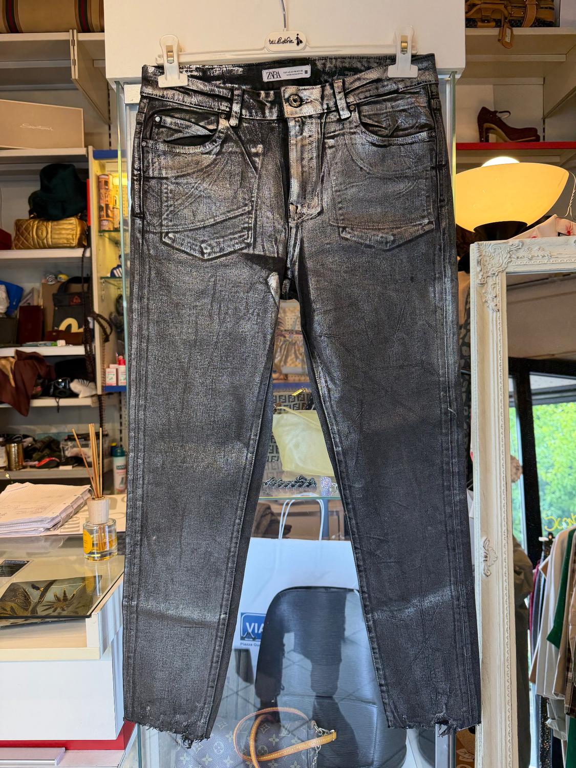 Metallic jeans hanging on a rail in a shop, with a background of shelves and various products. Visible tag: "ZARA".