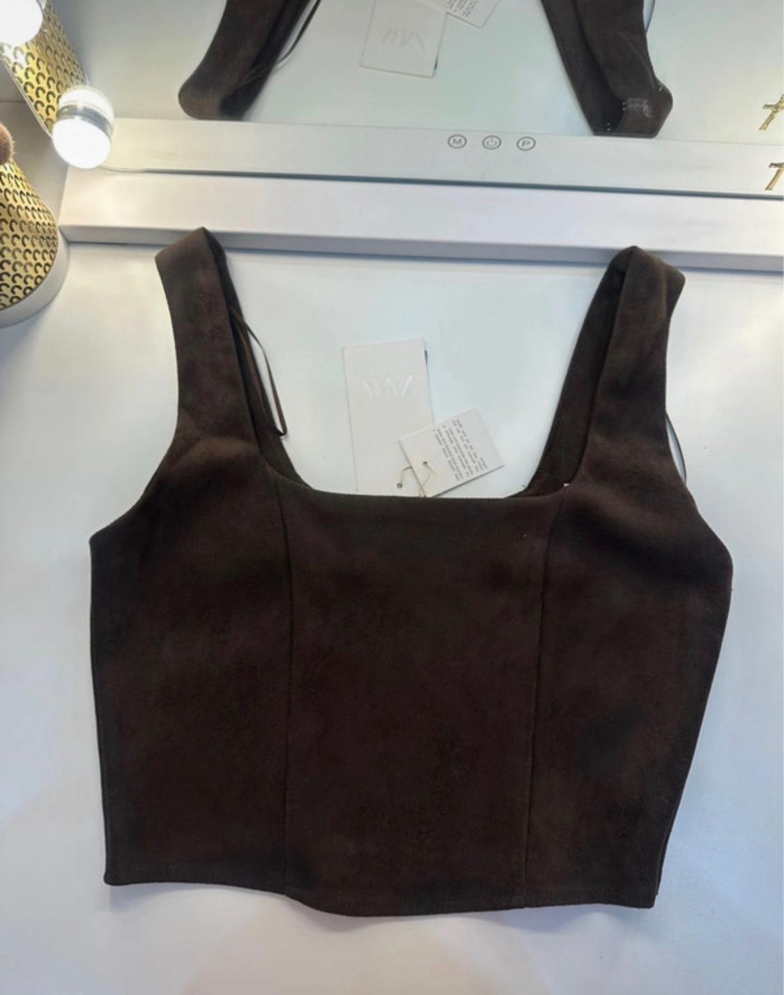 Dark brown square-neck cropped top with tags, on a white surface in front of a lighted mirror.