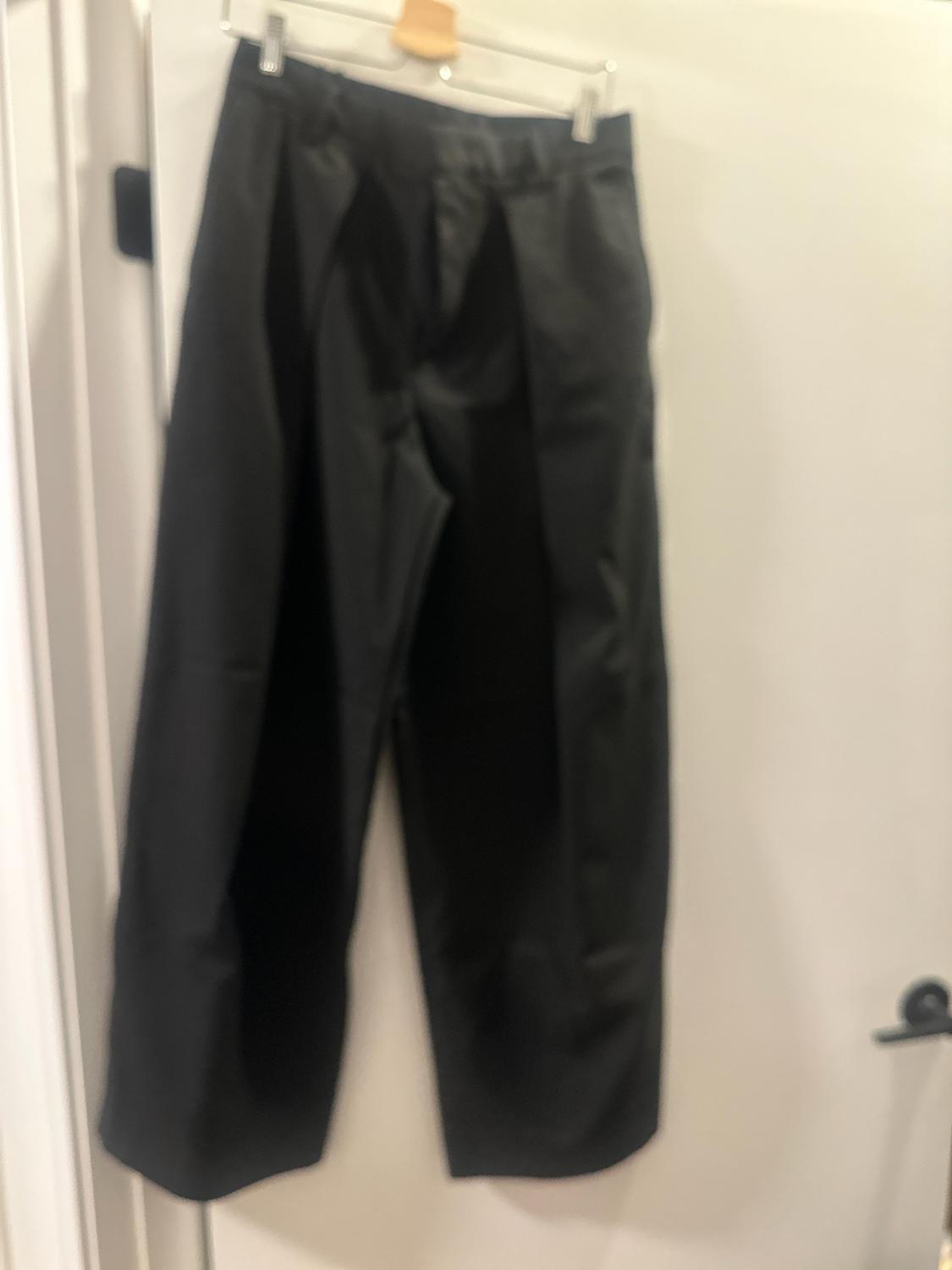 Wide black pants hanging on a hanger on a white door with a dark handle. Image with a relaxed and slightly out-of-focus style.
