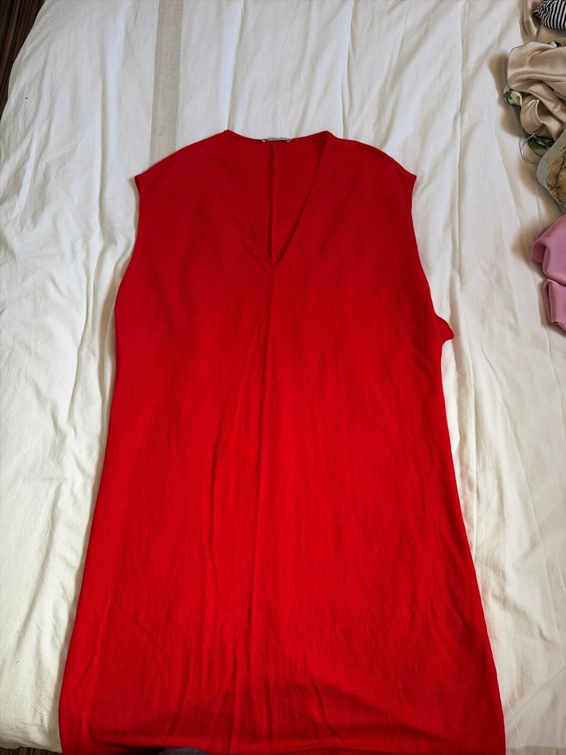 Sleeveless red dress with a V-neck, laid out on a rumpled white sheet in a relaxed setting.