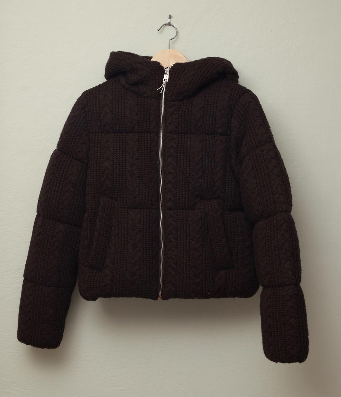 Dark brown quilted jacket with cable knit texture, hood and front zipper, hanging on a hanger against a light background.