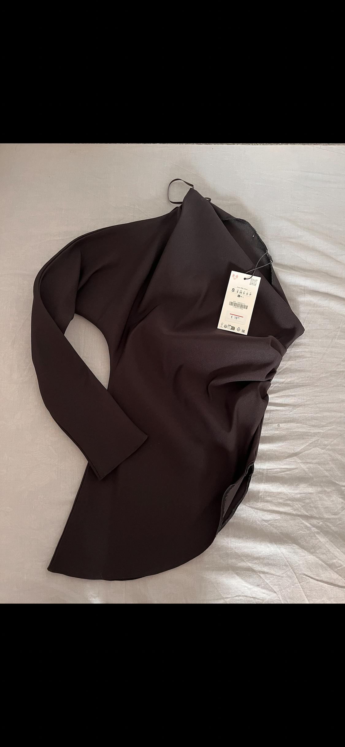 Black long-sleeved blouse on a light surface, with visible tag showing size S and price of €19.99.