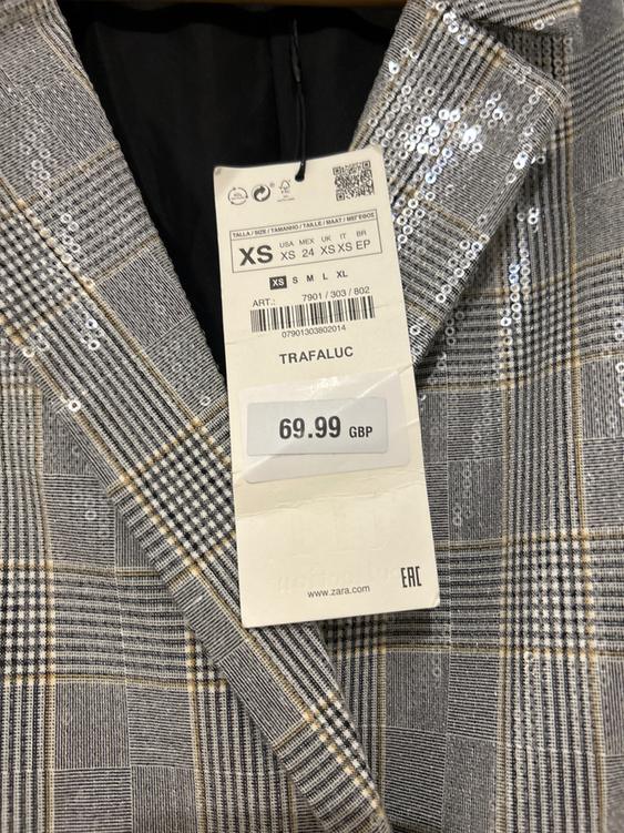 Price tag of GBP 69.99 on a sequined, checked jacket in grey and beige tones.