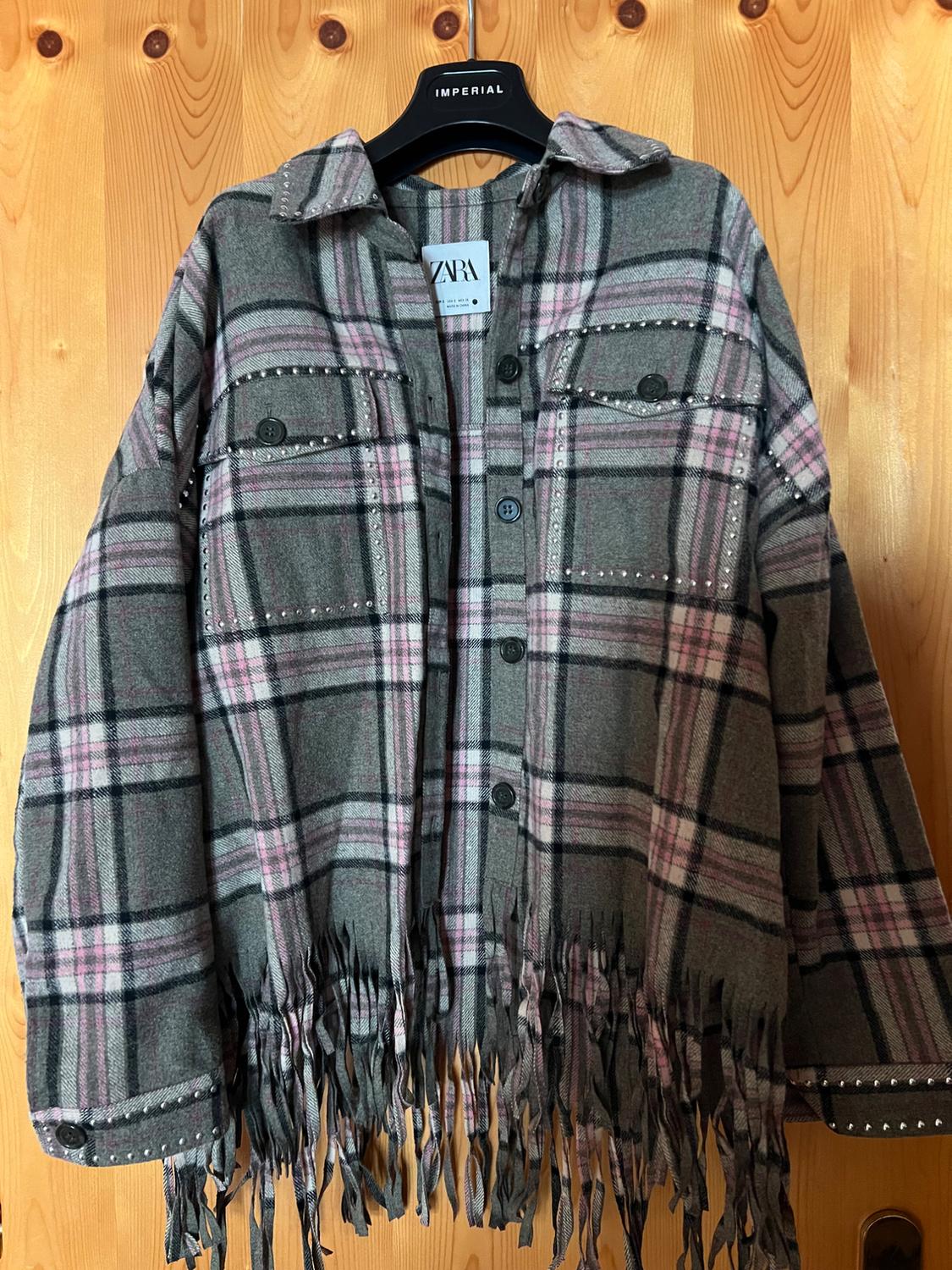 Grey and pink checked overshirt with studs and fringing, on an IMPERIAL hanger against a wooden background. ZARA label visible.