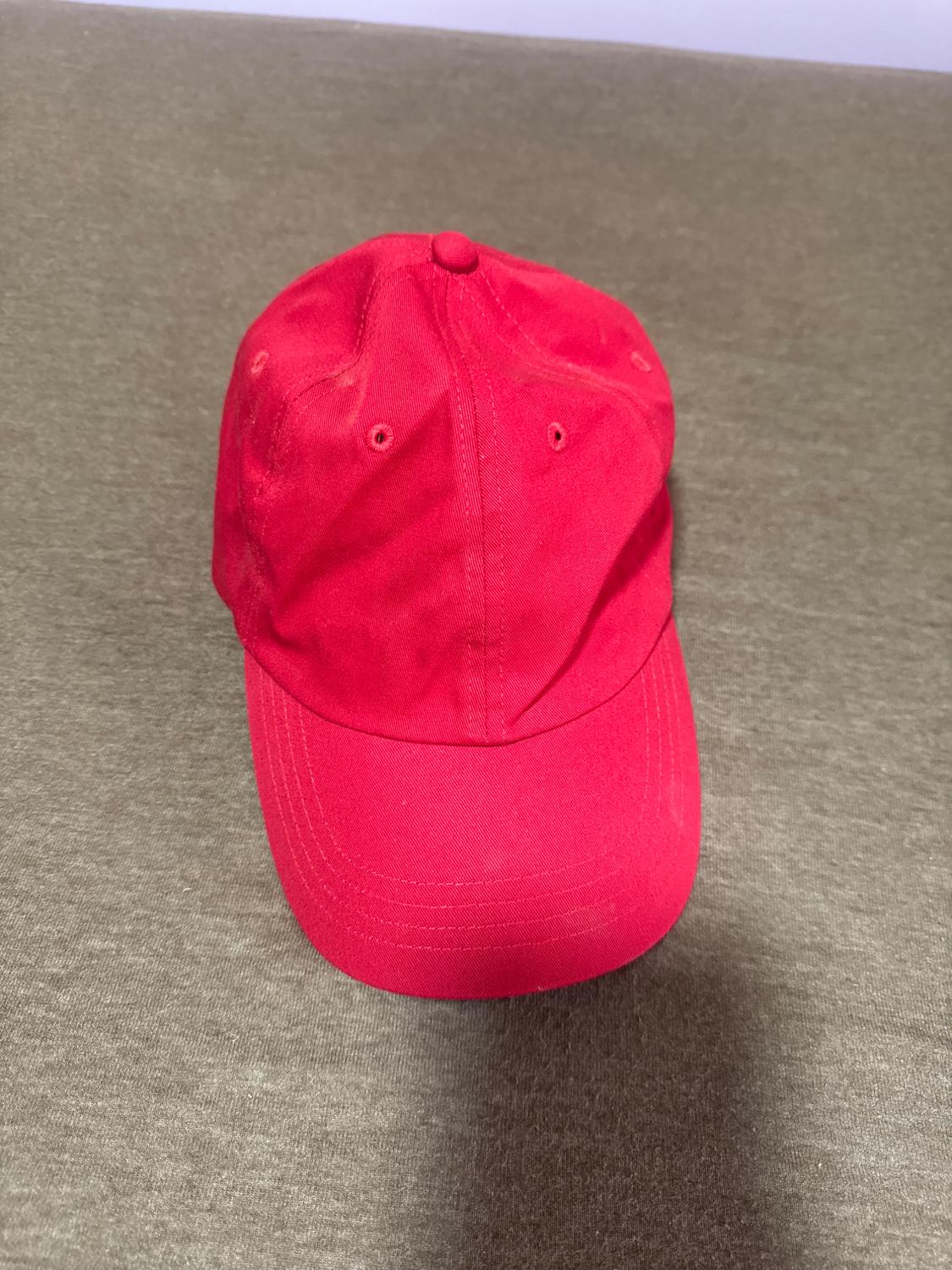 Red cap on a grey surface, viewed from above. The cap has visible stitching and a button on top.