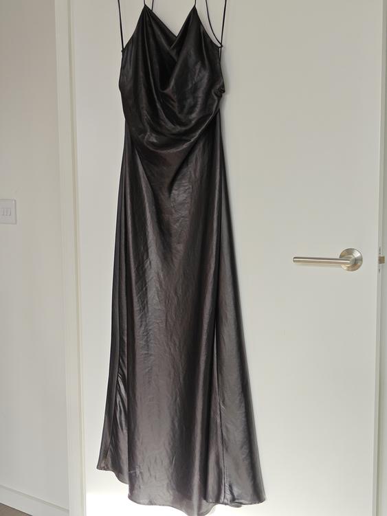 Black long dress with thin straps hanging on a white door, with a draped design on the neckline.