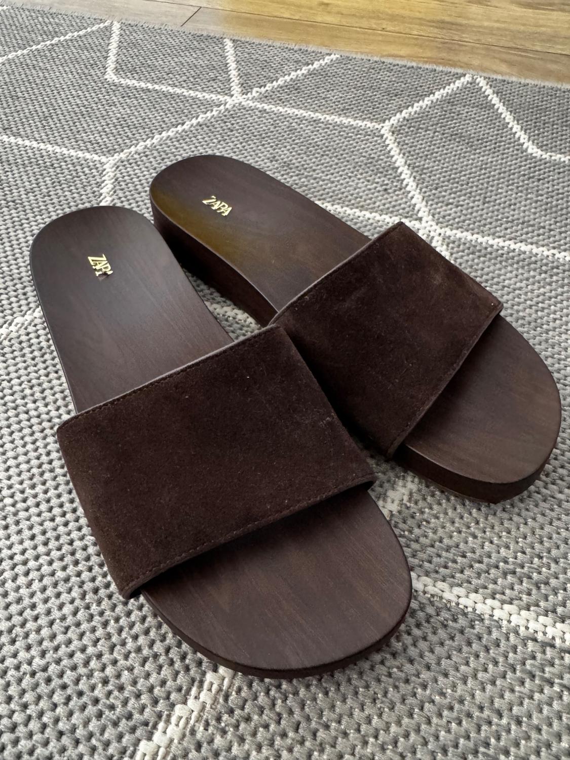 Brown wide-strap sandals with a wooden sole on a grey rug with a white pattern. ZARA text on the insole.