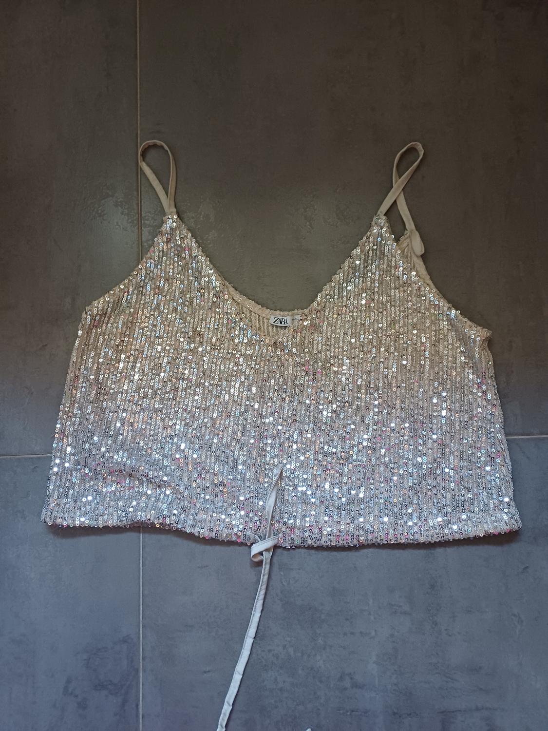 Silver sequin strappy top with a drawstring hem, laid out on grey tiles. Label with the text ZARA.