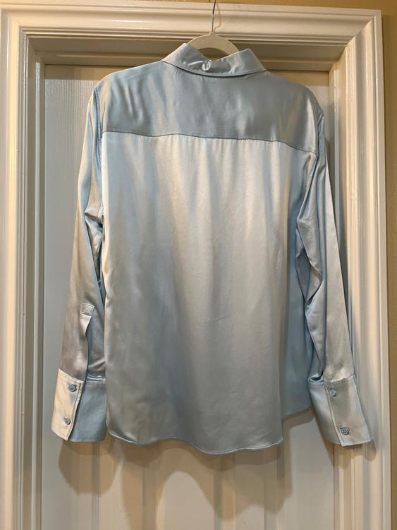 Light blue satin shirt hanging on a hanger over a white door. The shirt has a classic collar and buttoned cuffs.