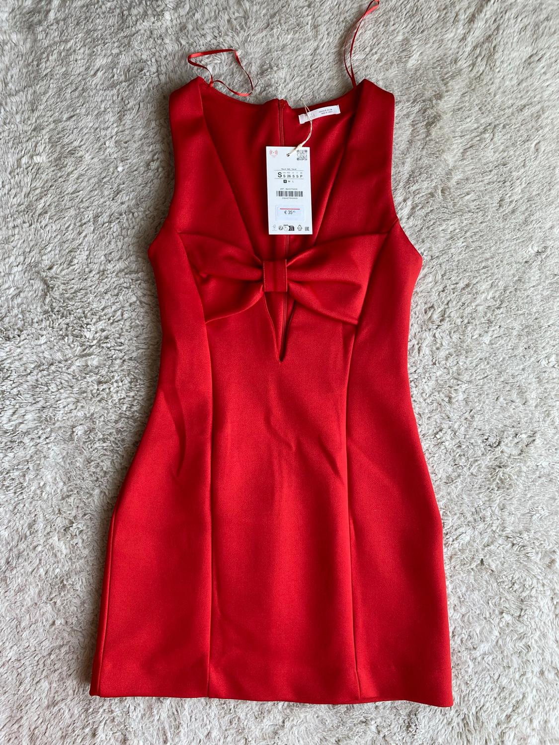 Red sleeveless dress with a deep neckline and front tie, on a fluffy rug. Label with text S and € 35.