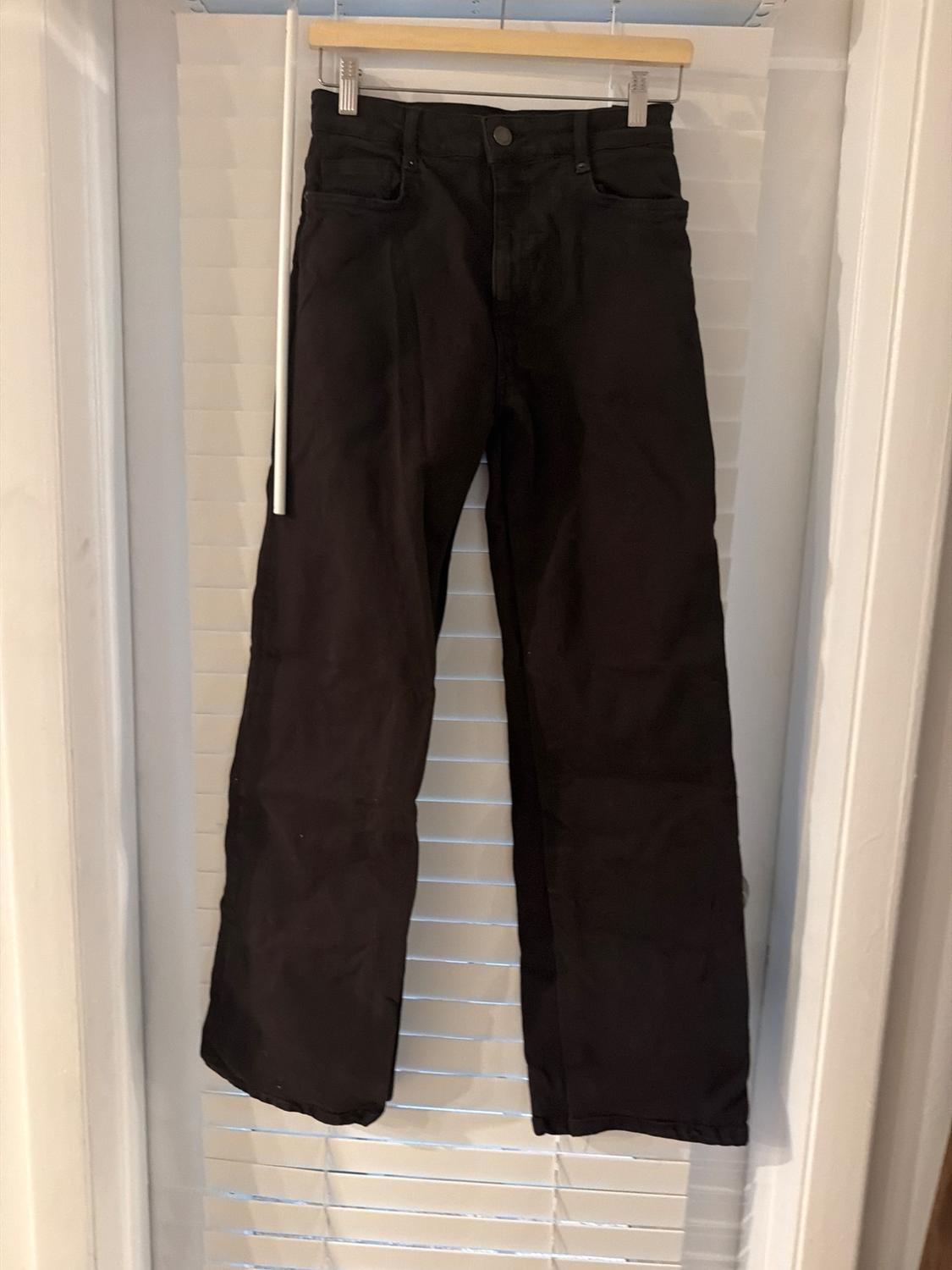 Black straight-leg pants hanging on a hanger in front of white blinds. Casual and relaxed style.
