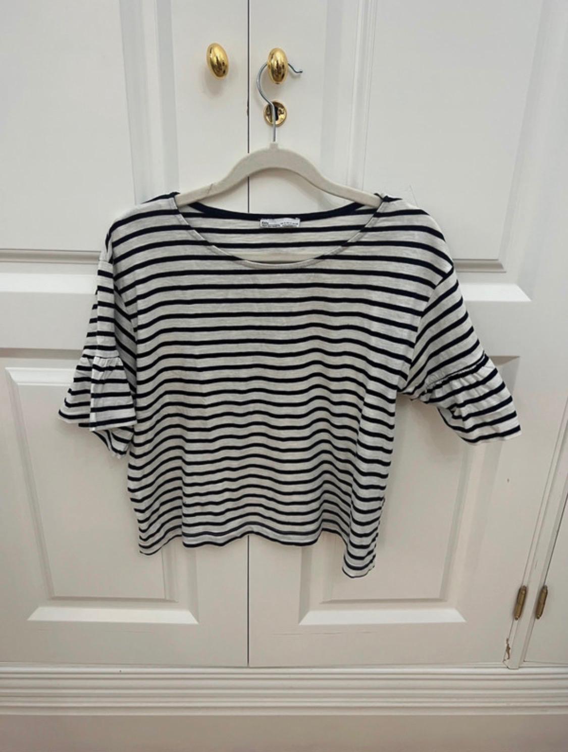 Black and white striped t-shirt with frill sleeves, hanging on a hanger over a white door with gold handles.