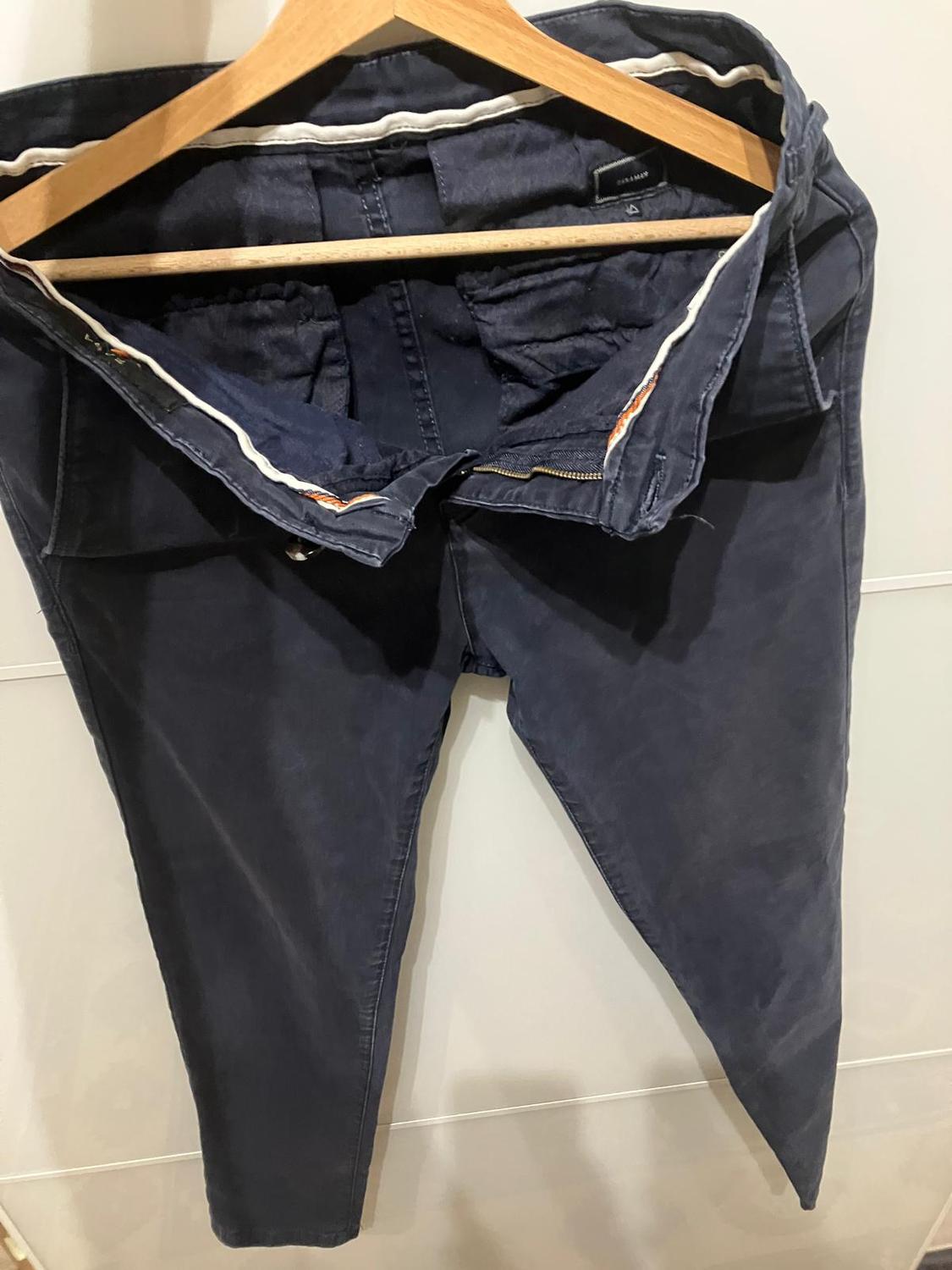 Dark blue trousers hung on a wooden hanger, showing the inside and the label visible at the top.