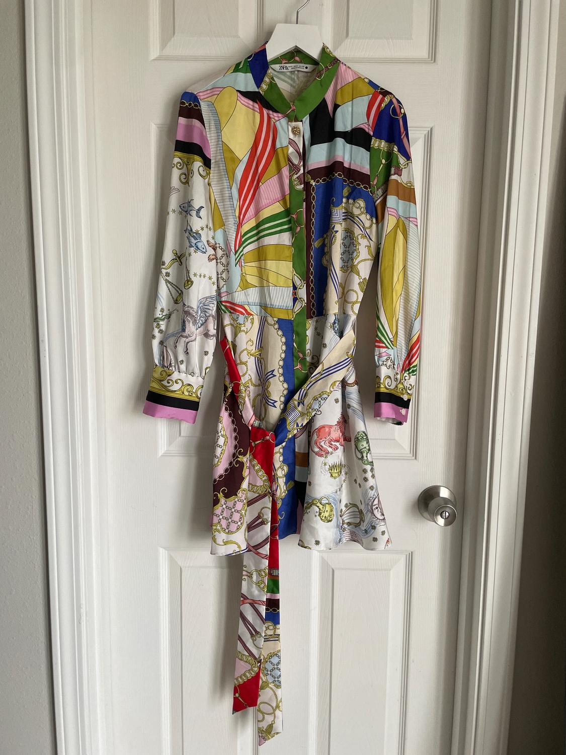 Colourful dress with a geometric and chain print, hanging on a white door. Includes matching belt.