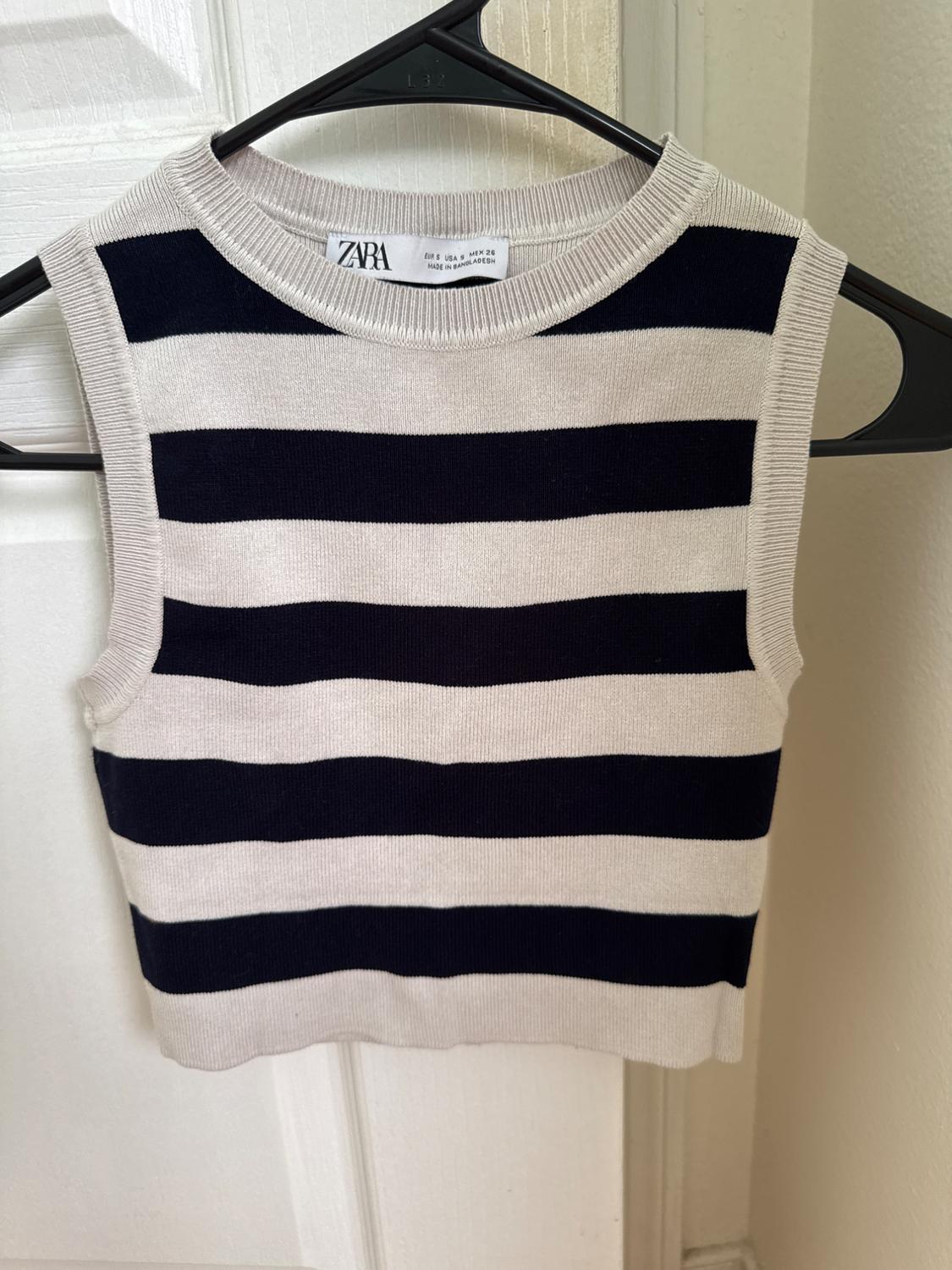 Front view of a black and white striped sleeveless t-shirt hanging on a hanger.