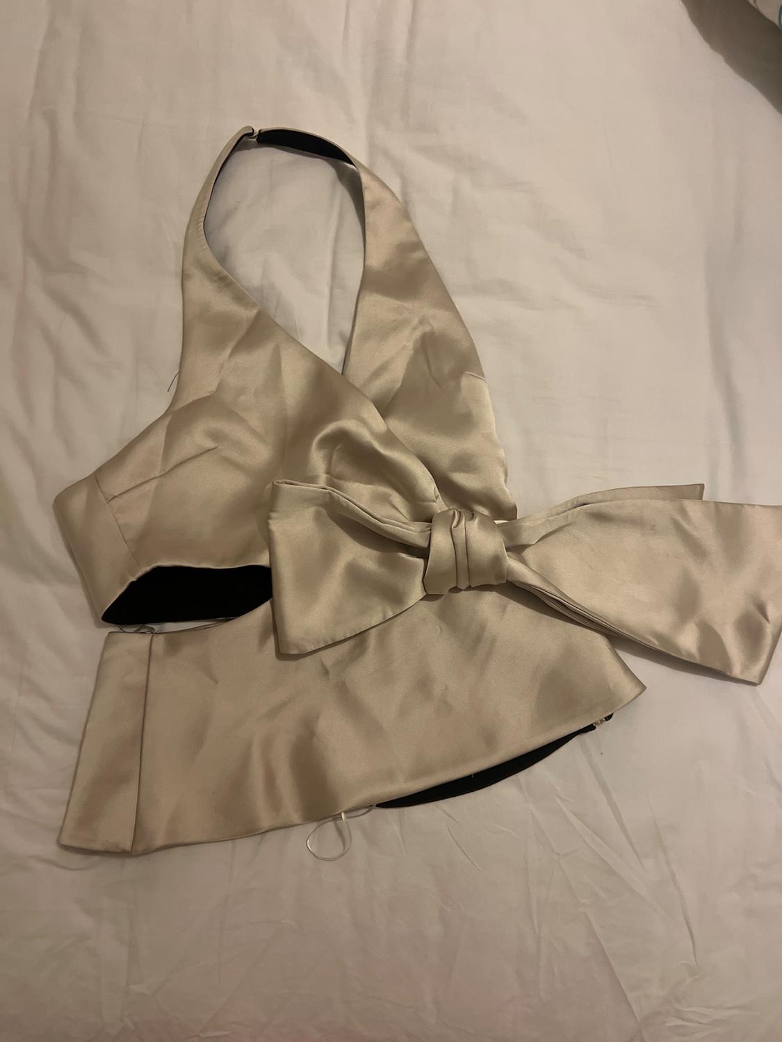 Beige satin halter neck top with a large bow on the front, on a white surface.