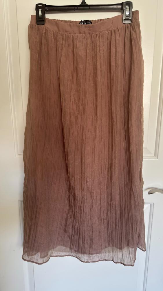 Light brown pleated long skirt hanging on a black hanger over a white door.
