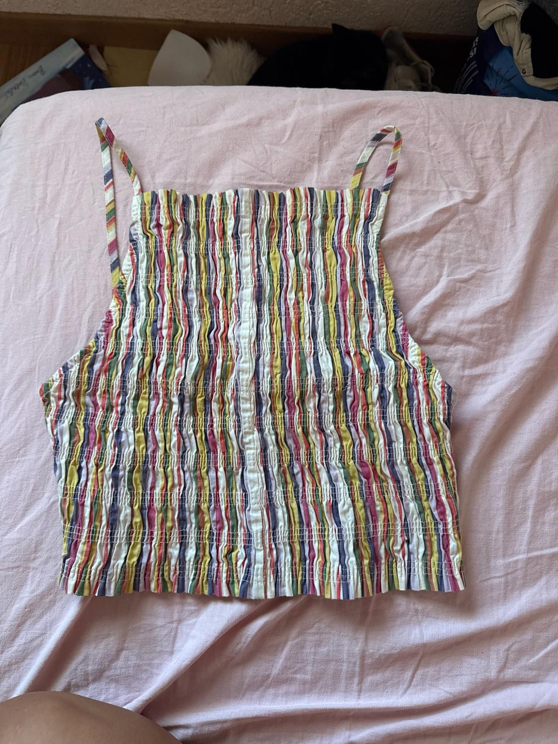 Cropped camisole top with shirred fabric and multicoloured vertical stripes, laid on a pale pink sheet in a relaxed setting.