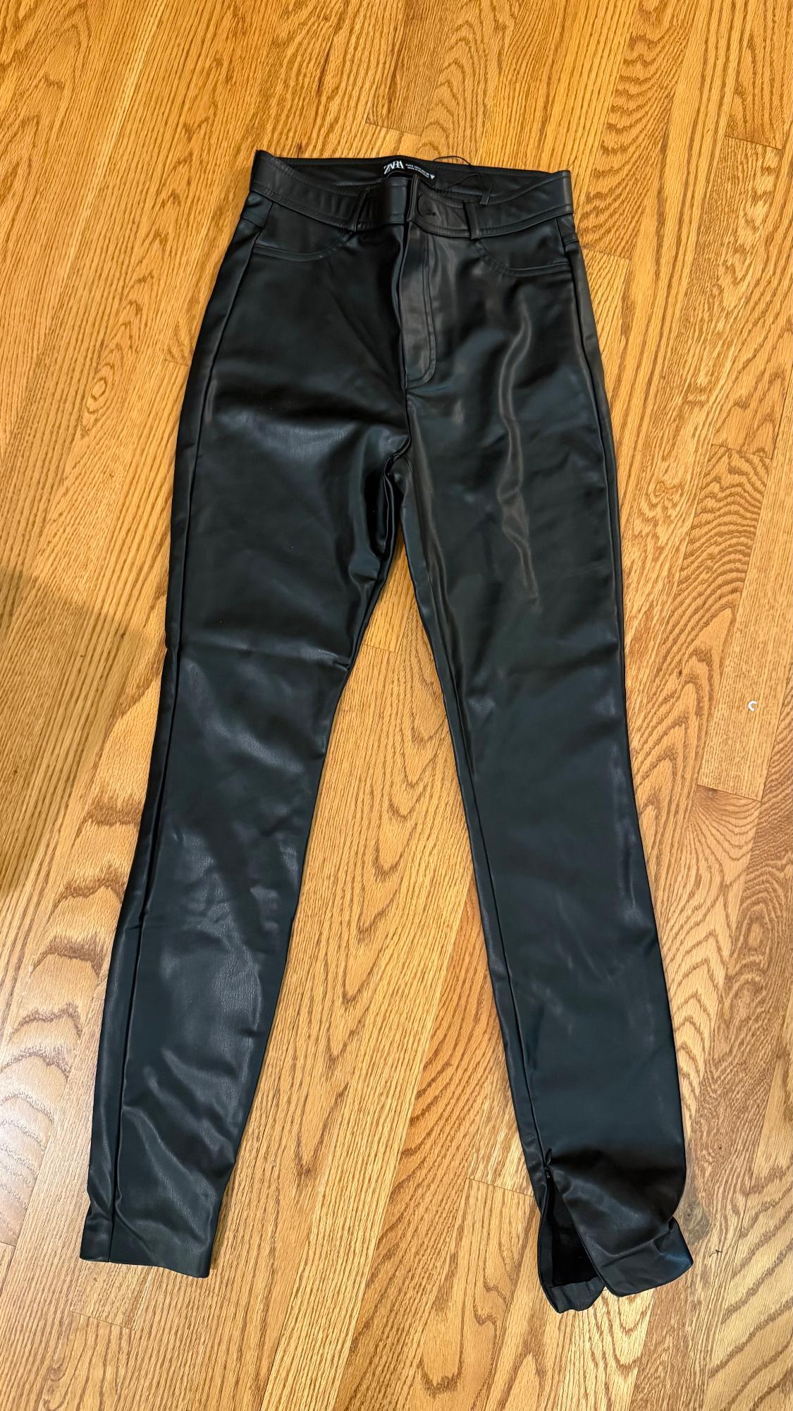 Black synthetic material pants on light wood floor. Visible label on the waistband.