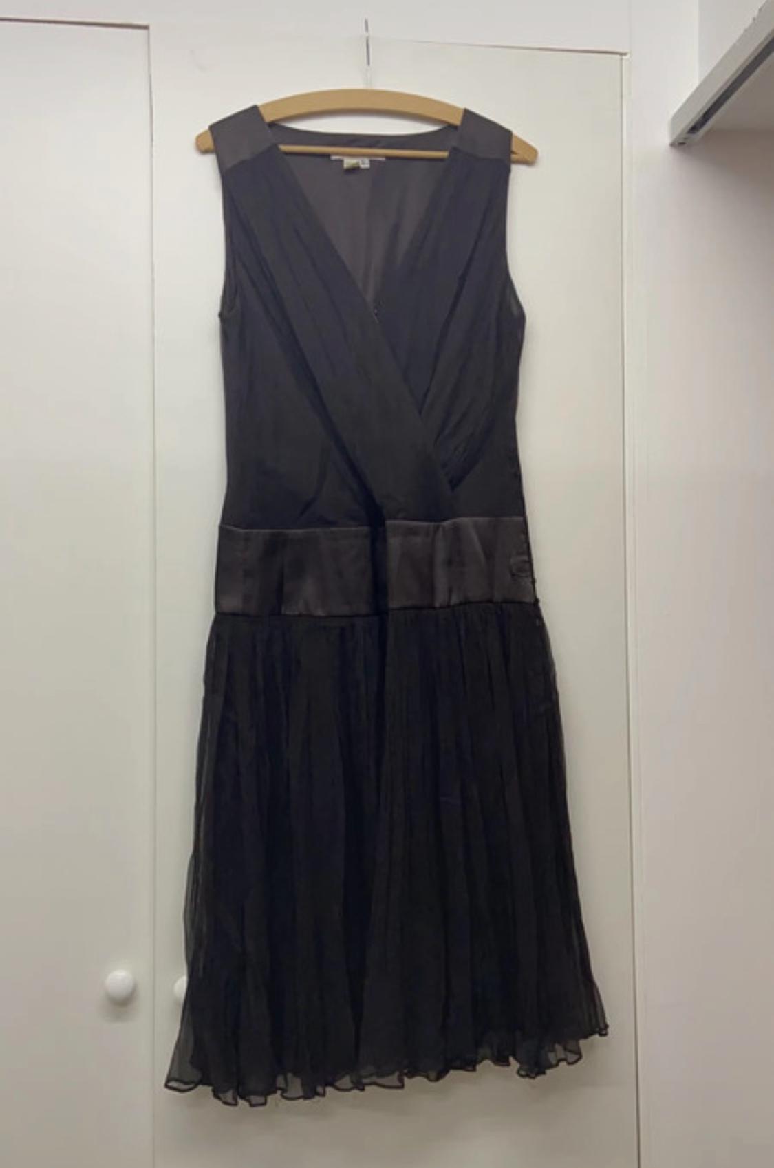 Front view of a black dress with a V-neck and a pleated skirt. Wide belt at the waist.