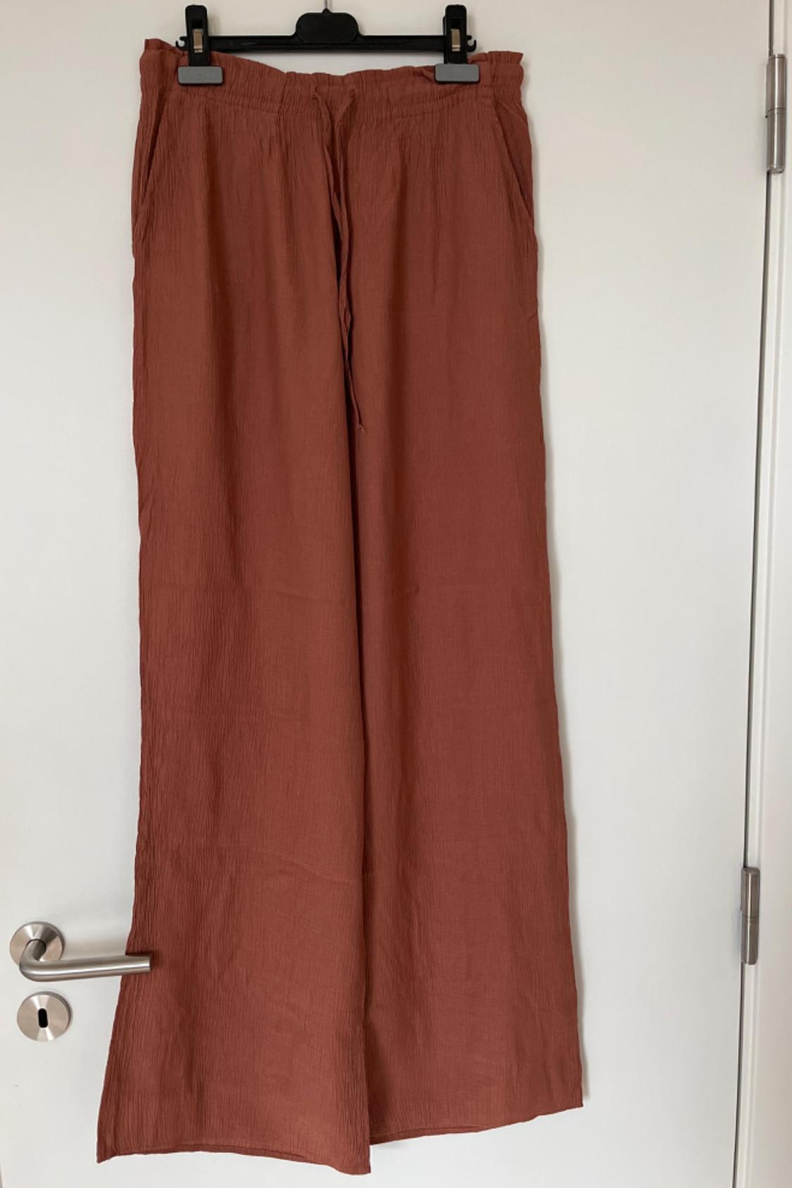 Front view of brown trousers with elasticated waistband and side pockets.