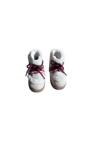 A pair of white winter boots with plush lining, burgundy-colored laces, and small multicolored flower embellishments on the front.