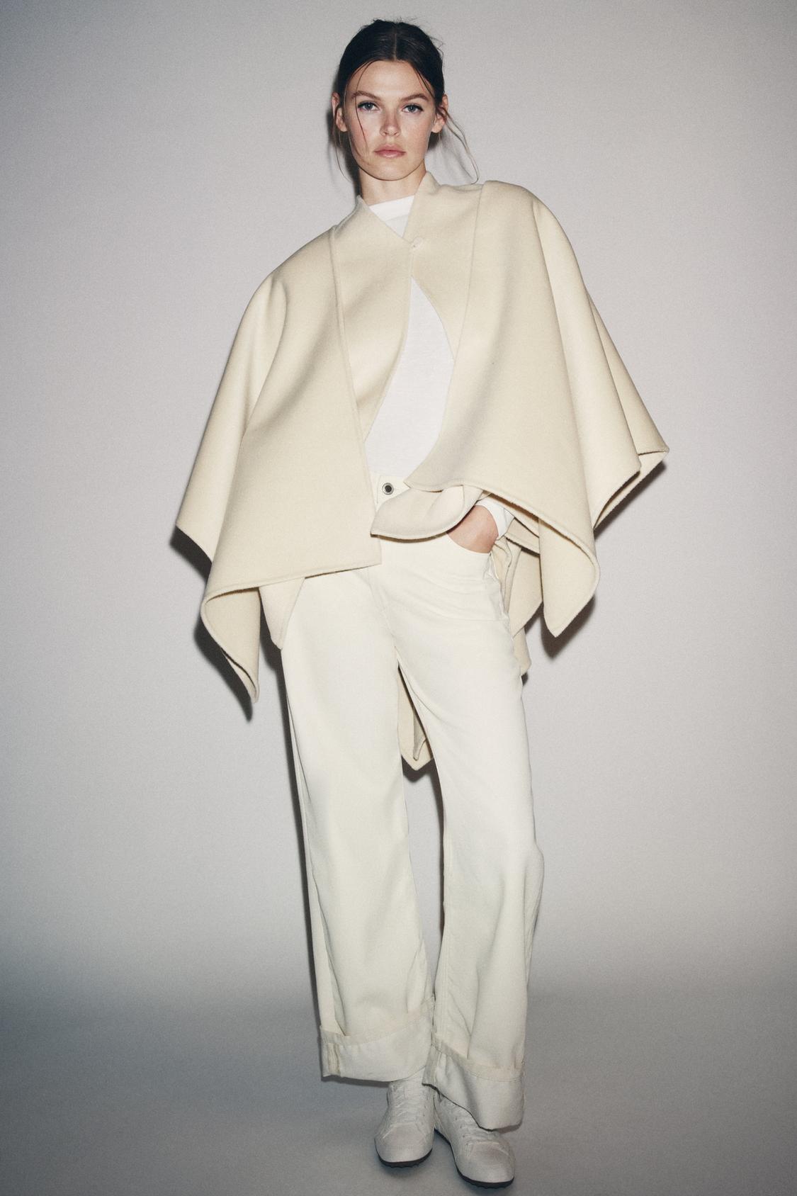 Komplet suknjiča-ogrinca v barvi ecru z okroglim ovratnikom in ravnimi hlačami. Vidni našiti žepi.