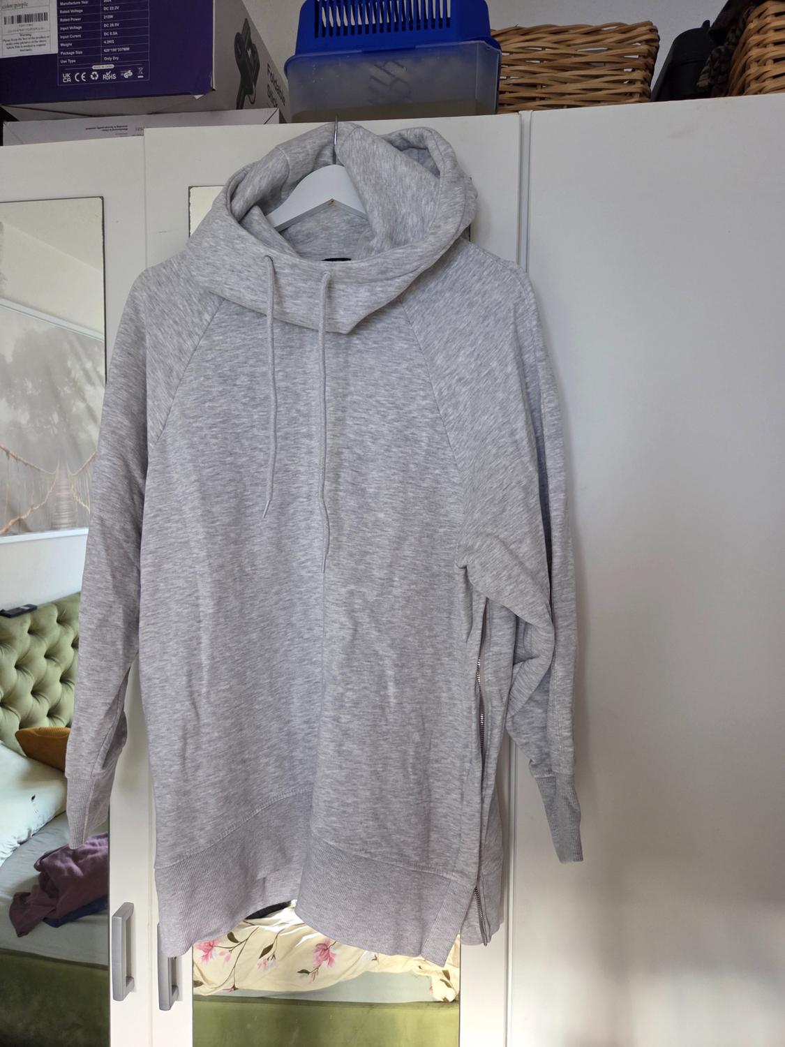 Light grey hooded sweatshirt with drawstrings and a side zip, hanging in a white mirrored wardrobe inside a bedroom.