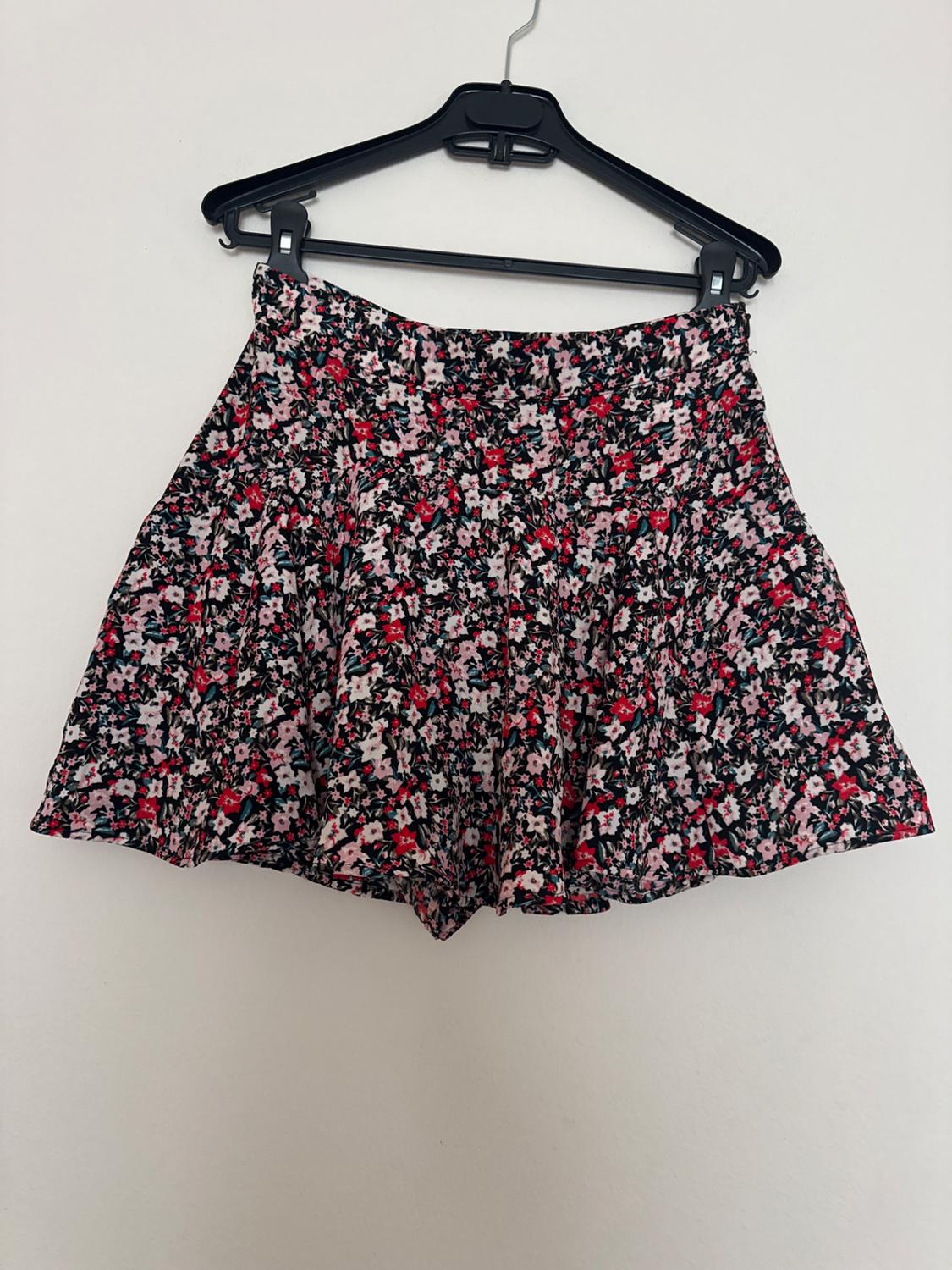 Short skirt with a floral print in shades of pink, red, and black, hanging on a black hanger against a white background.