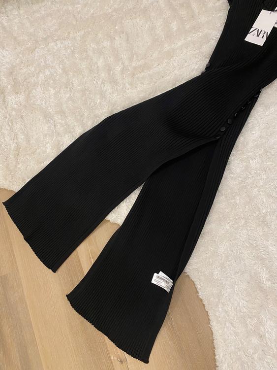 Black ribbed pants with side buttons on a white rug and wooden floor. Visible tag with text "ZARA".
