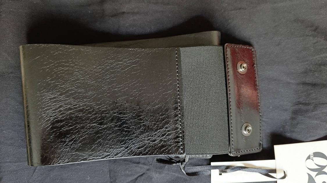 Close-up of a wide, glossy, textured black belt with an elasticated panel and press-stud fastening against a dark fabric background.