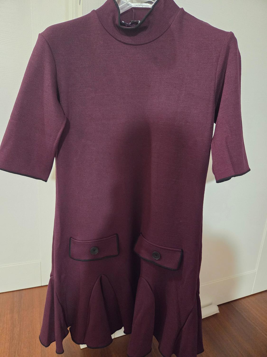 Burgundy short-sleeved dress with a high neck and decorative button pockets, hanging on a hanger against a white background.