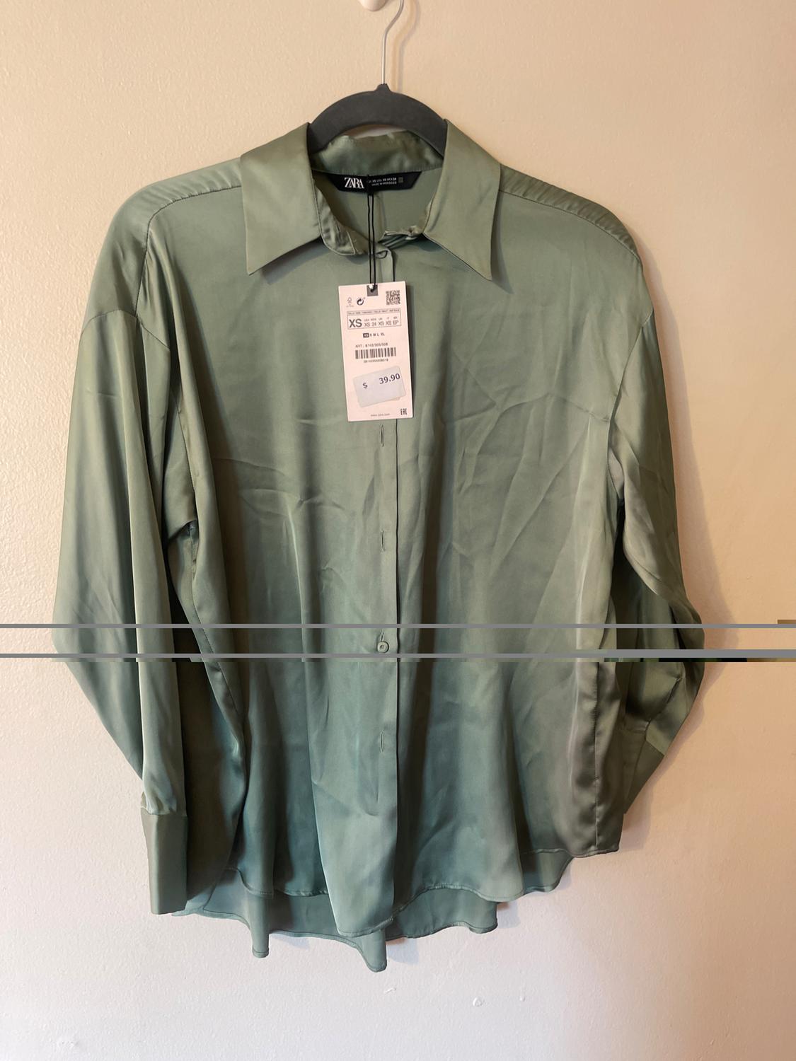 Long-sleeved green shirt hanging on a black hanger. Visible tag with price 39.90 and size XS. White background.